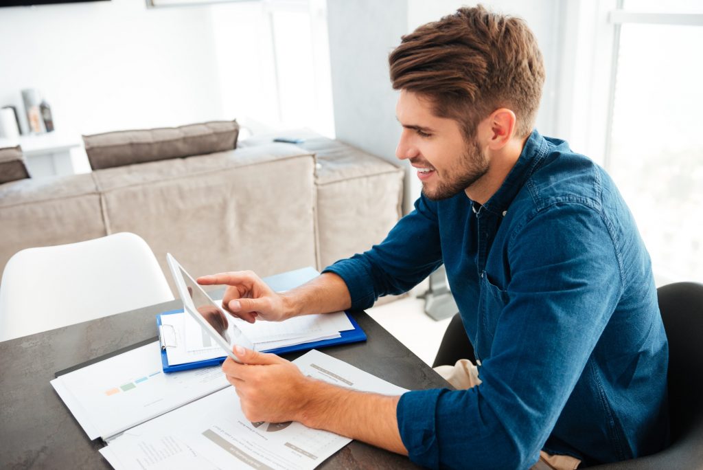 Happy young man sitting at table and holding tablet