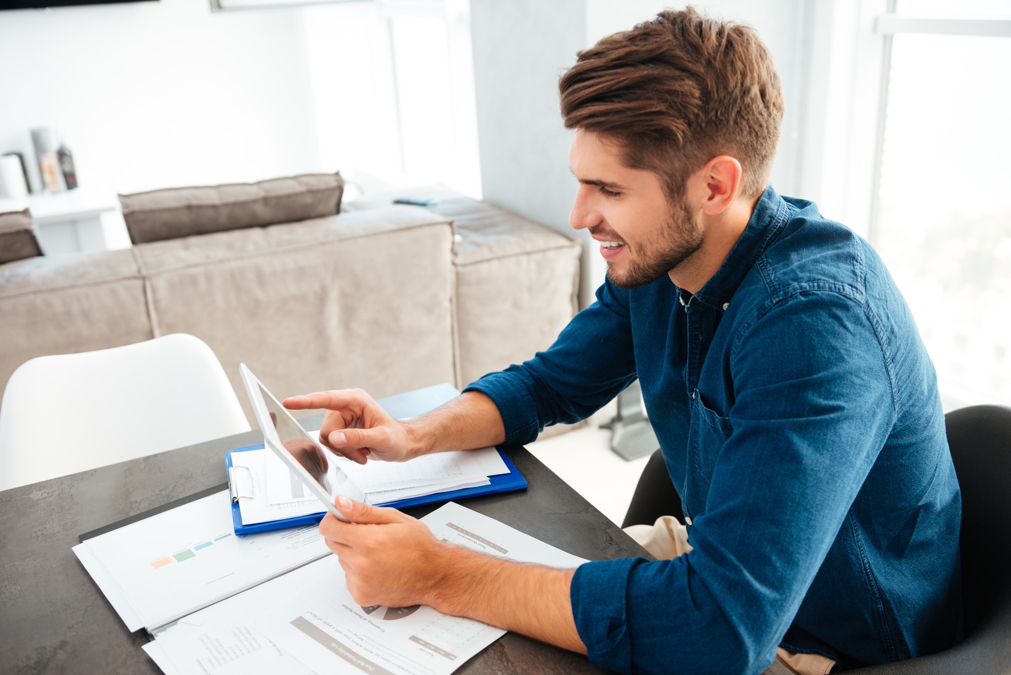 Happy young man sitting at table and holding tablet